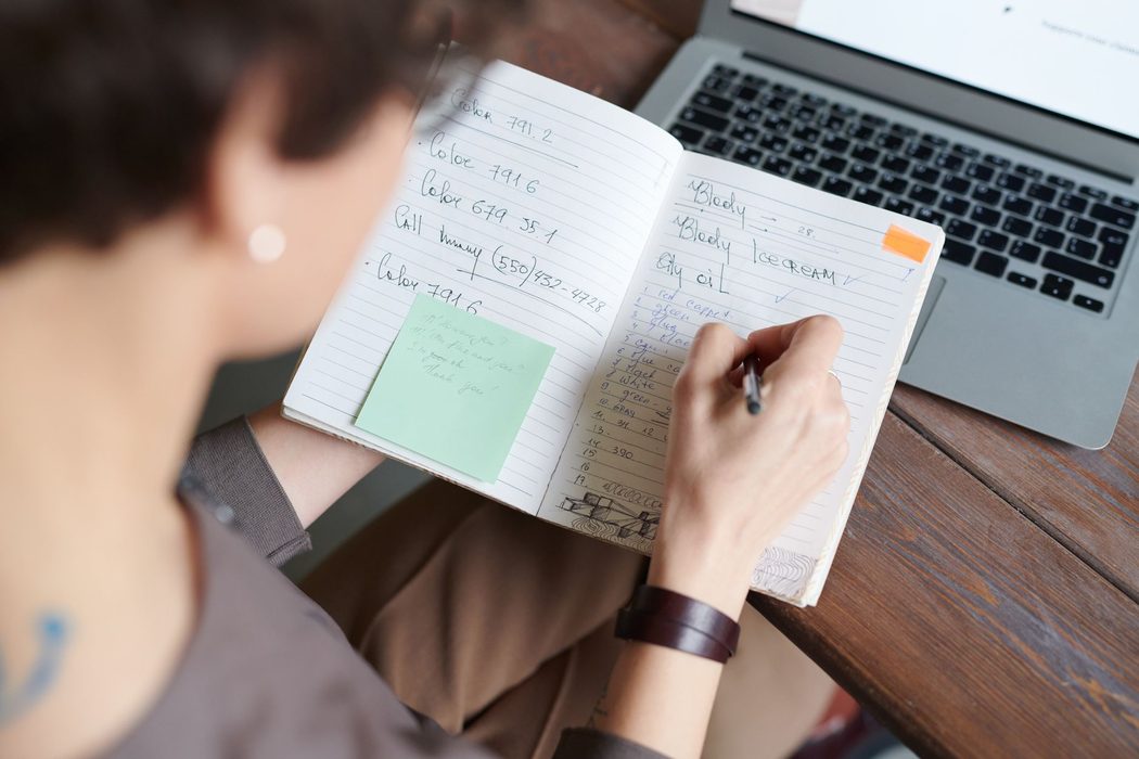Editor reviewing written notes beside a laptop while preparing an article