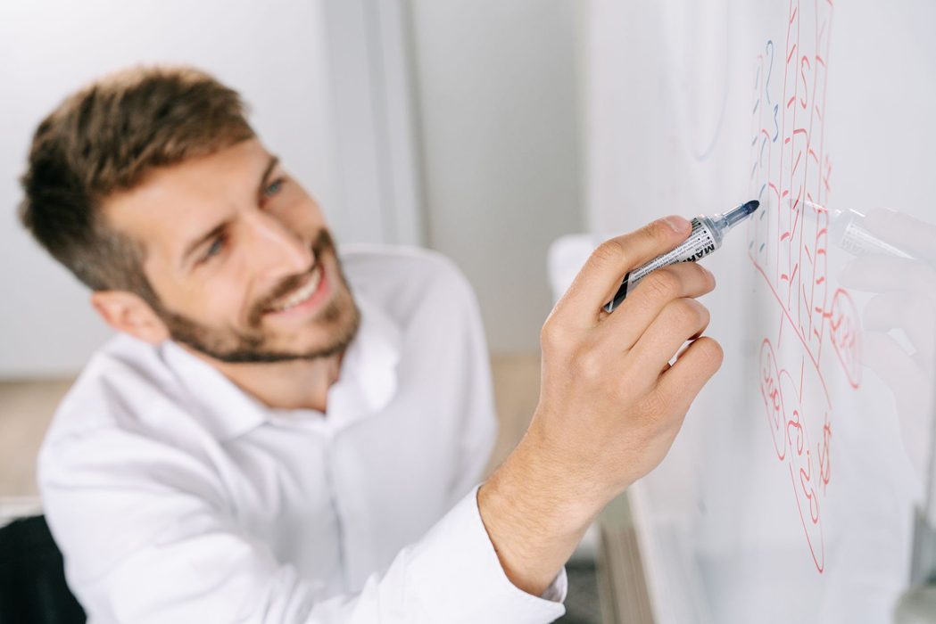 A person sketching a process diagram of boxes and arrows on a whiteboard